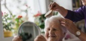 An elder smiling while receiving gentle personal care assistance
