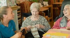 A caregiver sharing a warm moment with two women knitting